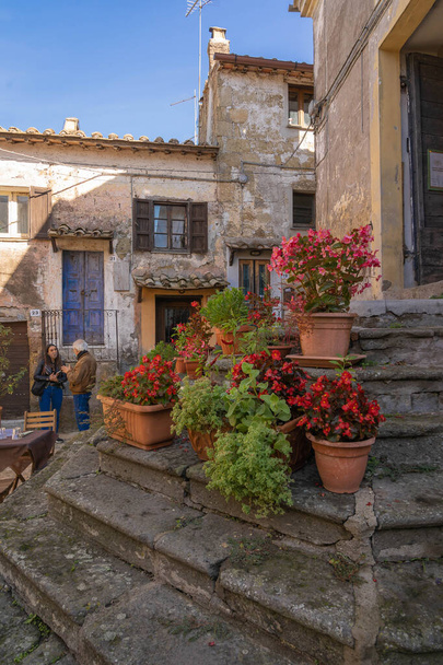 Calcata Vecchia, Italy - October 20, 2020, Masked people on stone steps with a lot of flowers of Calcata Vecchia, Italy. Second wave of coronavirus (covid19), keeping social distance - Foto, Imagen