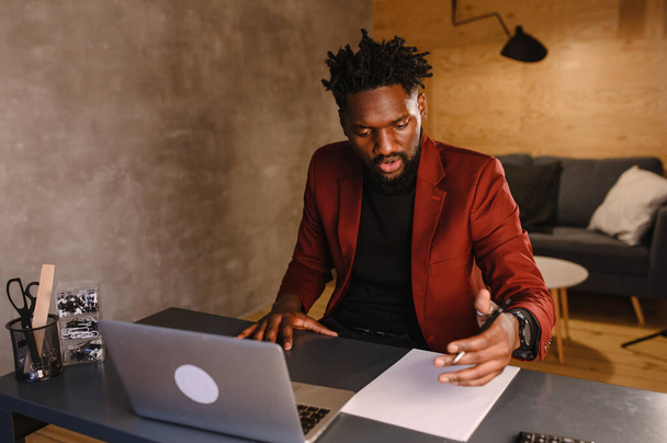 Focused young african businessman wear headphones study online watching webinar podcast on laptop listening learning education course conference calling make notes sit at work desk, elearning concept - Foto, Imagem