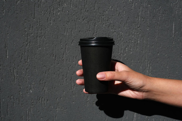 κορίτσι που κρατάει ένα μαύρο οικολογικό ποτήρι καφέ σε σκούρο φόντο. ποτά ντελίβερι - Φωτογραφία, εικόνα