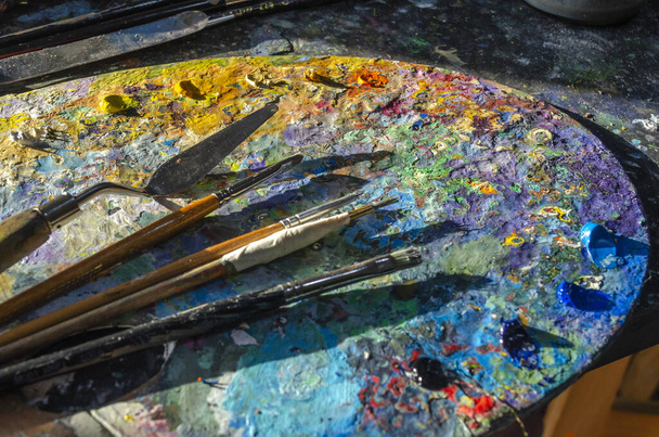 Stock Photo of a painter brushes and palette knife on a palette with mixed and unmixed oil colours with sunlight - Fotografie, Obrázek