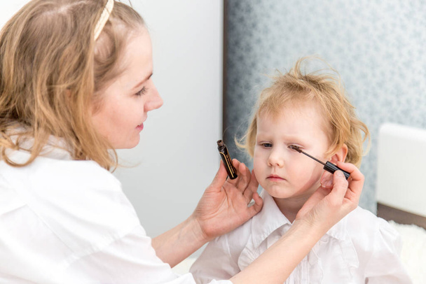 Portrait of woman doing makeup to her daughter in the bedroom on the bed. - 写真・画像