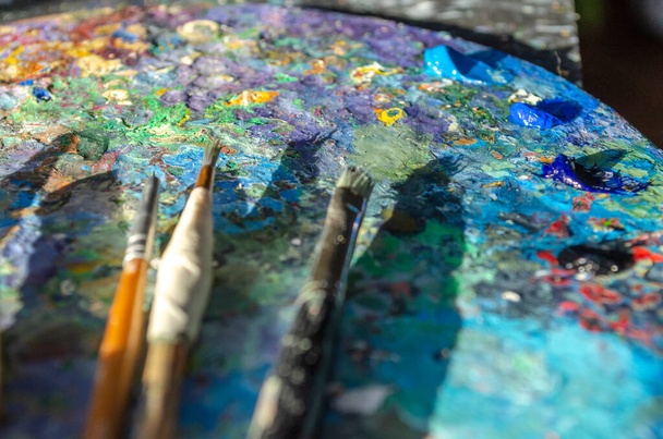 Stock Foto van een schilder penselen en palet mes op een palet met gemengde en ongemengde olieverf met zonlicht - Foto, afbeelding