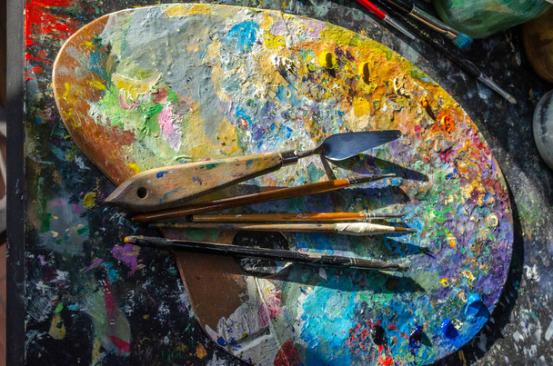 Stock Photo of a painter brushes and palette knife on a palette with mixed and unmixed oil colours with sunlight - Photo, Image