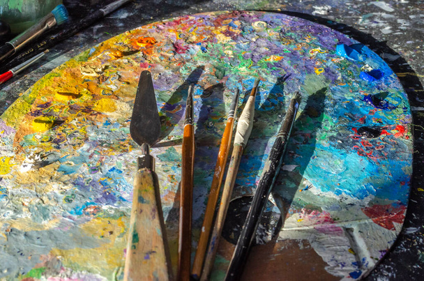 Stock Photo of a painter brushes and palette knife on a palette with mixed and unmixed oil colours with sunlight - Foto, afbeelding