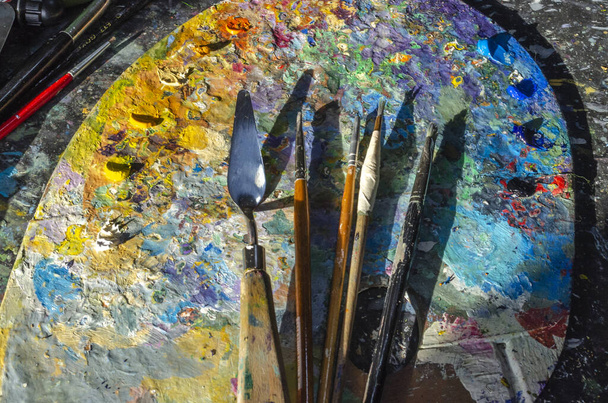 Bir ressamın palet üzerindeki fırça ve palet bıçağının güneş ışığıyla karışık ve karıştırılmamış yağlı renkleri. - Fotoğraf, Görsel