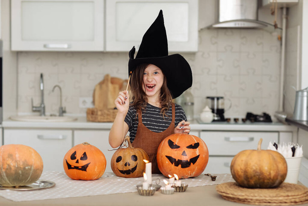 Happy halloween. Cute little girl in witch costume with carving pumpkin. Happy family preparing for Halloween. girl lights candles. - Fotografie, Obrázek