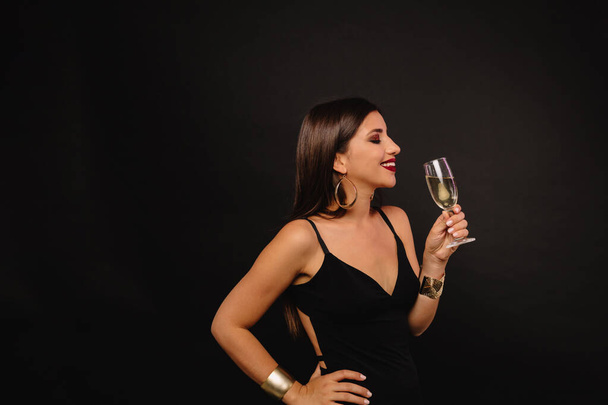 Retrato de perfil de mujer elegante y elegante en vestido negro bebiendo champán sobre fondo negro. Foto de alta calidad - Foto, Imagen