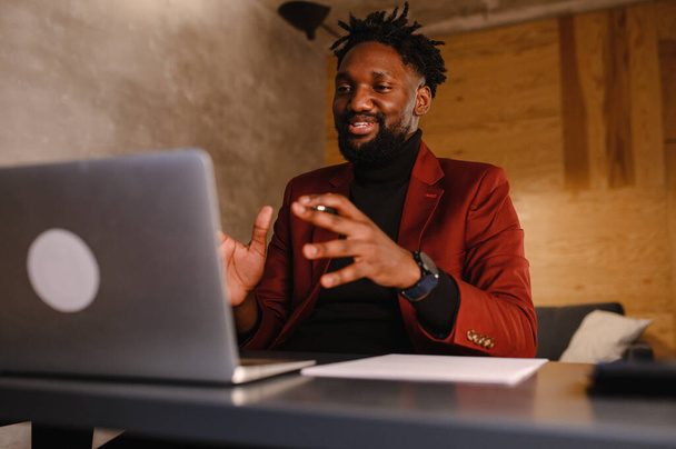 Focused young african businessman wear headphones study online watching webinar podcast on laptop listening learning education course conference calling make notes sit at work desk, elearning concept - Photo, Image