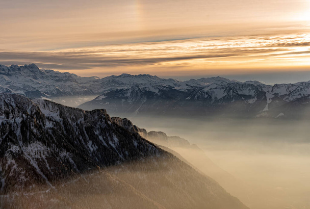 日没の霧に覆われた山の雪の冬の風景。スイスのローチャーズ・ド・ナエ. - 写真・画像