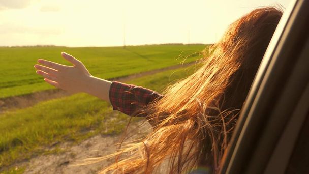mujer libre viaja en coche coge el viento con la mano desde la ventana del coche. Chica con el pelo largo está sentado en el asiento delantero del coche, estirando su brazo por la ventana y la captura de resplandor de puesta de sol - Foto, Imagen