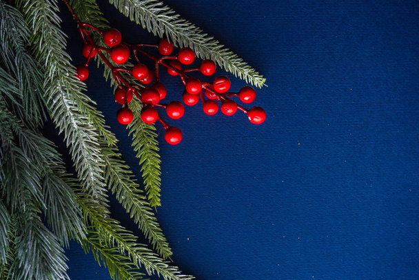 Marco de Navidad con rama de árbol y bayas rojas sobre fondo azul profundo - Foto, Imagen