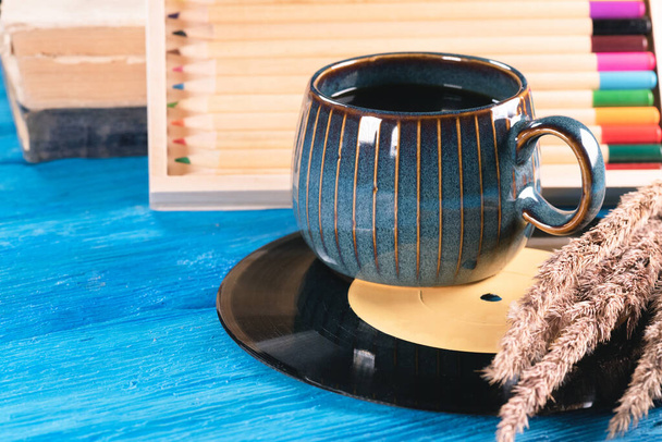 Black coffee cup, vinyl record, book and colorful pencils on the blue wooden table background. - Photo, Image