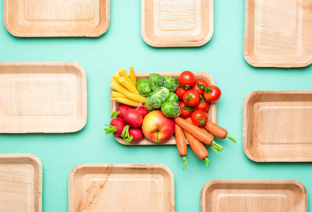Top view with fresh vegetables in a zero-waste tray. Eco-friendly palm leaf plates on a green-colored background. - Photo, Image