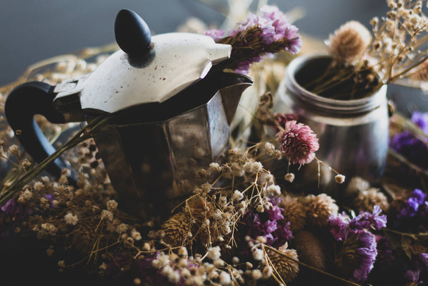 Σκέψη για καφέ. Υλικά για την παρασκευή καφέ moka. Moka κατσαρόλα με καφέ σε σκούρο φόντο με πολλά πολύχρωμα λουλούδια. Ο καφές είναι σε vintage αισθητική σύνθεση. - Φωτογραφία, εικόνα