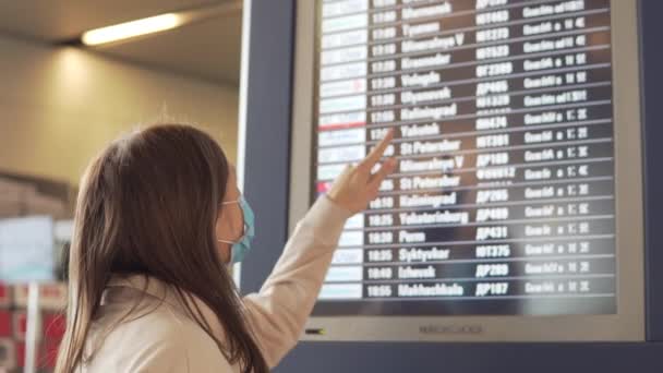 Kobieta w masce medycznej stoi na lotnisku przy tablicy odlotów podczas pandemii covid-19. - Materiał filmowy, wideo