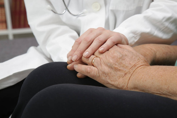 Przyjazny lekarz trzymający starszych pacjentów za rękę dla zachęty, empatii i wsparcia po badaniu lekarskim. Koncepcja zaufania i etyki medycznej.  - Zdjęcie, obraz