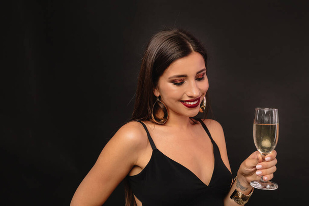 Sisäuima studio muotokuva onnellinen ihana nainen lasi viiniä kultainen korvakorut mustalla taustalla. Laadukas kuva - Valokuva, kuva