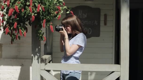 Ένα ευγενικό νεαρό κορίτσι στέκεται στην είσοδο του καφέ και προσαρμόζει την κάμερα επιλέγοντας την καλύτερη γωνία για τη φωτογραφία. Μπροστά. Μέσο σχέδιο - Πλάνα, βίντεο