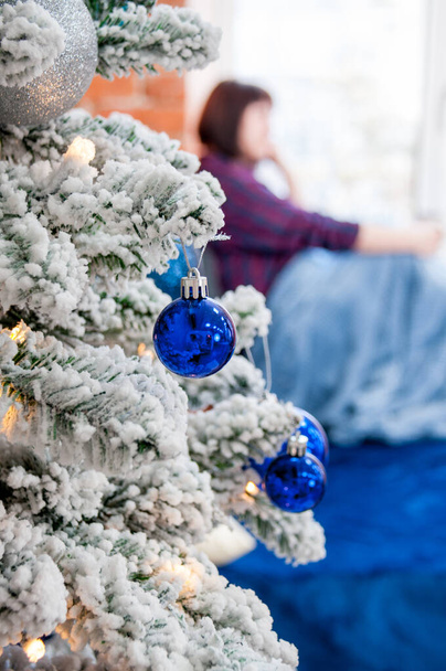Zarif bir Noel ağacının parçası ve bulanık bir kadın kışın, yeni yılın sabahında sıcak ve rahat bir evde pencerenin kenarında oturuyor. - Fotoğraf, Görsel