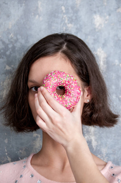 A girl in a pink blouse holds a doughnut on her hand near her eye close up - Valokuva, kuva