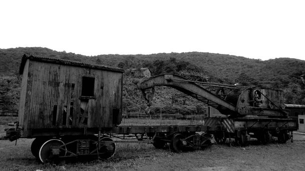 Stary, zardzewiały i opuszczony wagon umieszczony na polu trawiastym ze wzgórzami za nim (czarno-biały) - Zdjęcie, obraz