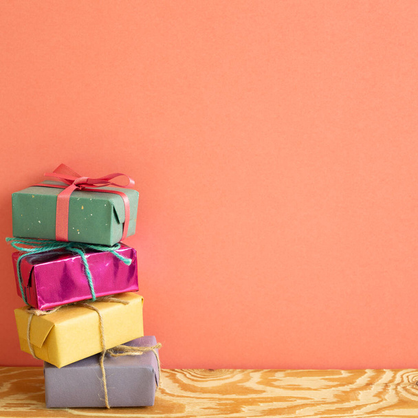 Stapel von bunten Geschenkboxen auf Holztisch mit korallenrosa Hintergrund - Foto, Bild