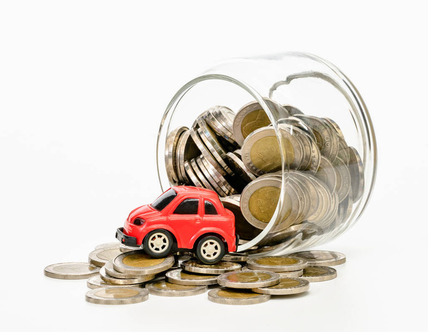 monedas en botella de vidrio y coche rojo sobre fondo blanco, ahorro de negocio y concepto de inversión - Foto, imagen