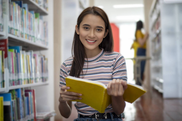 Asiatische Studentinnen lächeln, lesen ein Buch und machen Hausaufgaben in der Bibliothek - Foto, Bild