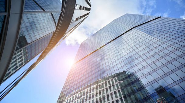 Untere Ansicht moderner Bürogebäude im Geschäftsviertel. Wolkenkratzer-Glasfassaden an einem strahlend sonnigen Tag mit Sonnenstrahlen am blauen Himmel. - Foto, Bild
