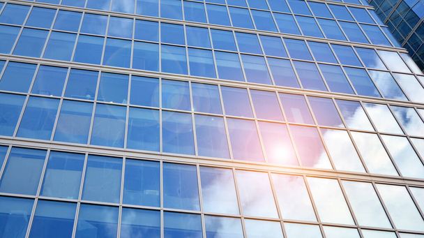 Blauwe gordijnwand gemaakt van gehard glas en stalen constructies onder blauwe hemel. Een fragment van een gebouw. Glazen gevels op een zonnige dag met zonnestralen aan de blauwe hemel. - Foto, afbeelding