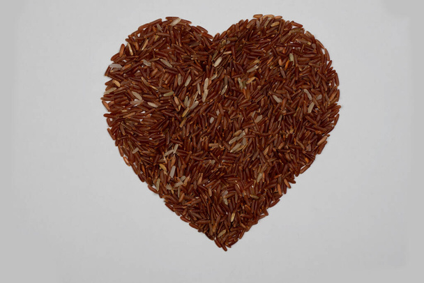 Brown rice kernels, stacked together in a heart shape, on a white background. - Photo, image