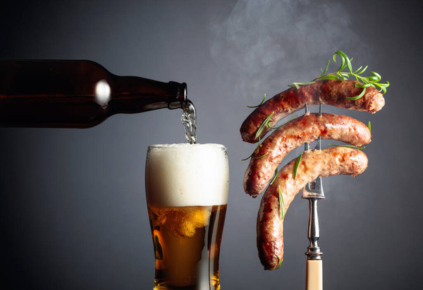 Beer and grilled Bavarian sausages. Juicy steaming sausages on a fork sprinkled with rosemary. Copy space. - Photo, Image