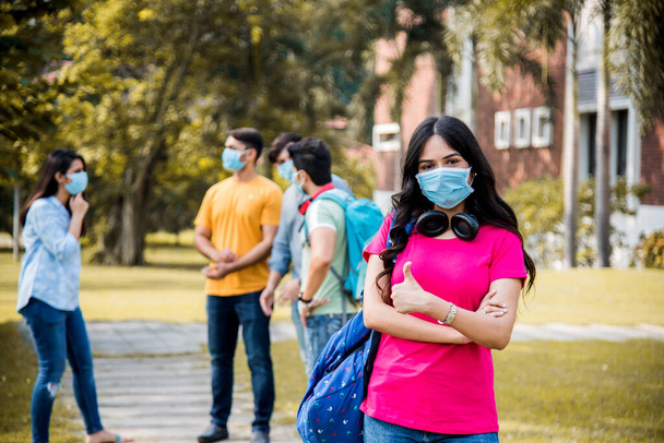 Asiatico indiano studenti indossa maschera viso e seguire le norme di distanza sociale in college o campus universitario dopo corona pandemia sbloccare, concentrarsi su uno studente - Foto, immagini