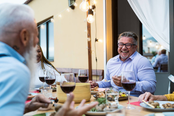Amigos seniores felizes se divertindo jantando juntos no pátio da casa - Conceito de estilo de vida de alimentos e idosos - Foto, Imagem