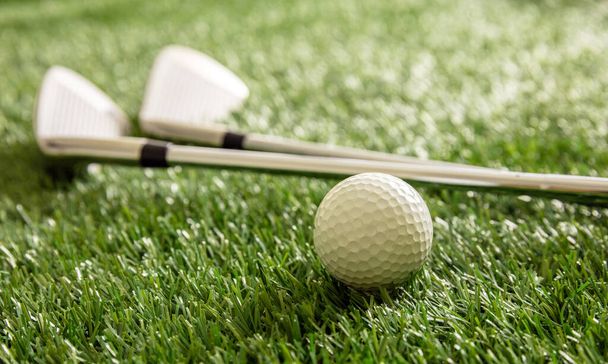 Golf ball and clubs on green course lawn, sunlight reflections, close up view. Golfing sport equipment concept. - Fotó, kép