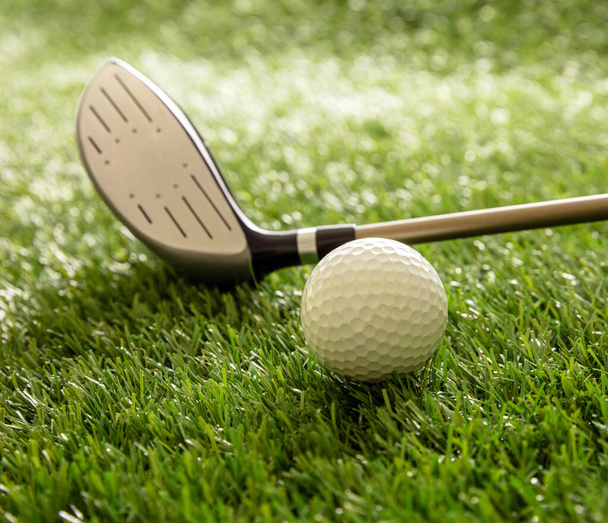 Golf topu ve golf sopası yeşil sahada, güneş ışığı yansımaları, yakın görüş. Golf malzemeleri ve kulüp konsepti. - Fotoğraf, Görsel