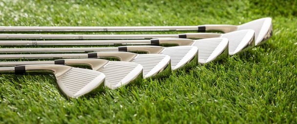 Golfclubs op groene baan gazon, zonlicht reflecties, close-up uitzicht. Golfsport en uitrusting concept, banner. - Foto, afbeelding