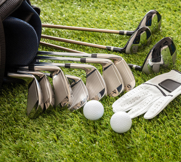 Golfové vybavení, hole zasazené do tašky rukavice a golfové míčky na trávníku, zblízka. Golfový sport a klubový koncept - Fotografie, Obrázek