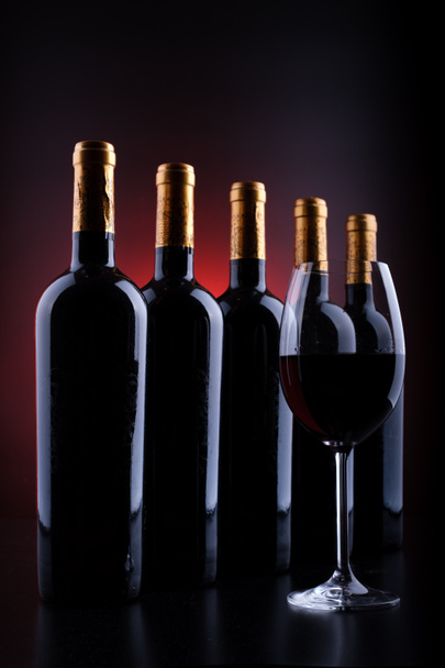 Weinflaschen und volles Glas mit rotem und schwarzem Silhouettenhintergrund - Foto, Bild