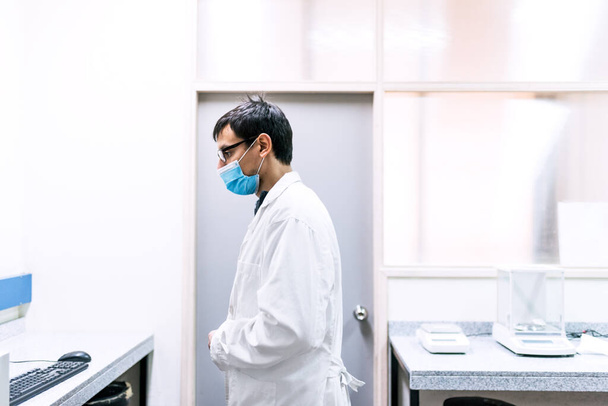 Фотография мужчины-ученого в маске для лица, работающего в лаборатории. - Фото, изображение