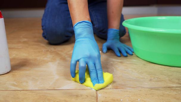 Blue-gloved hands scrub the marble floor using a sponge and detergent. - Foto, afbeelding