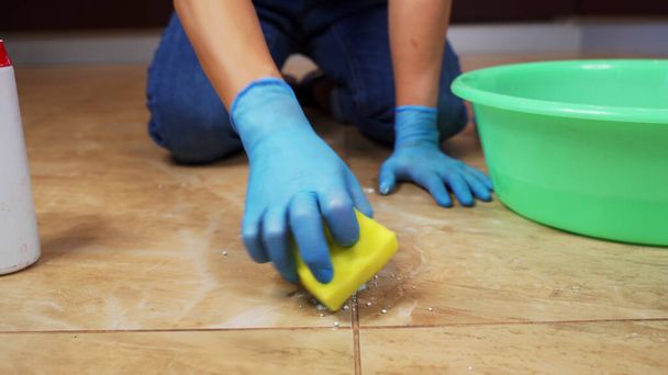 Blue-gloved hands scrub the marble floor using a sponge and detergent. - Фото, зображення