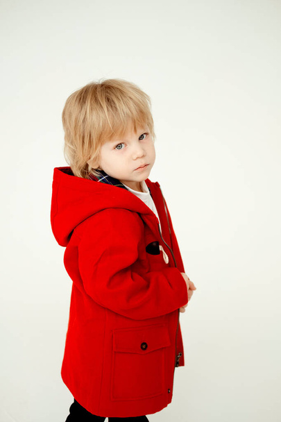 serious blond boy. The child is sad on a white background.Boy in red coat - Foto, imagen