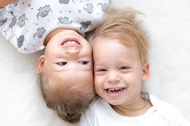 Trójka uśmiechniętych dzieciaków bawi się razem w łóżku. Szczęśliwy brat i siostra okazują emocje. Bliźniaki bawią się w domu na miękkiej białej kanapie. śmieszne rodzeństwo śmiać się i więzi z małą różnicą wieku.Kopiuj przestrzeń. - Zdjęcie, obraz