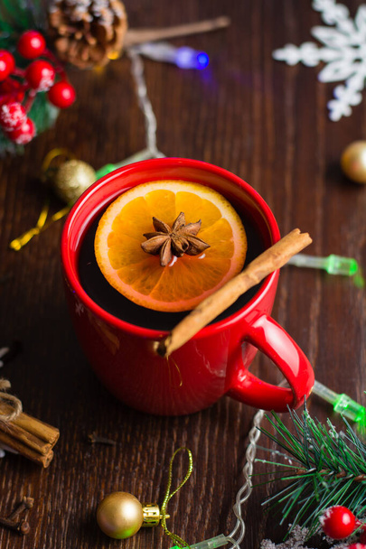 Νόστιμο ζεστό αλκοολούχο ποτό με κανέλα και αστεροειδή γλυκάνισο σε κόκκινο κύπελλο. Η έννοια της προετοιμασίας για τα Χριστούγεννα, ζεστασιά και άνεση στο σπίτι, κάθετη μορφή. - Φωτογραφία, εικόνα