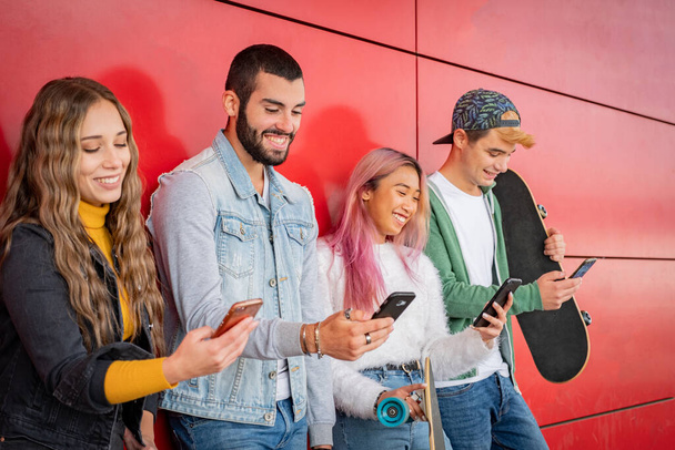 Groep jonge vrienden staren naar hun mobiele telefoons terwijl ze tegen een muur in de stad staan - Teneegers met behulp van smartphones - Foto, afbeelding