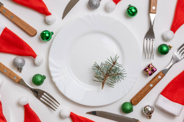 Traditional Christmas table place setting with empty white plate, linen napkin, cutlery with festive decorations. New Years background and Holiday concept. Flat lay, top view with copy space - Fotoğraf, Görsel