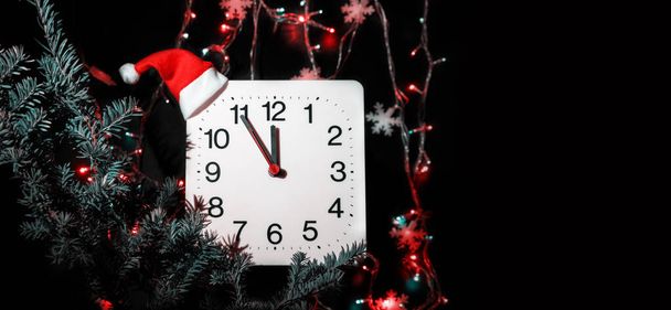 Uhr in Zweigen der Neujahrstanne auf schwarzem Hintergrund. Sekundenzeiger bewegt sich im Kreis der mechanischen Uhr und zeigt zwölf Uhr um Mitternacht und am Vorabend von Weihnachten. Urlaubskonzept, Zeitraffer, Nahaufnahme, Nahaufnahme - Foto, Bild