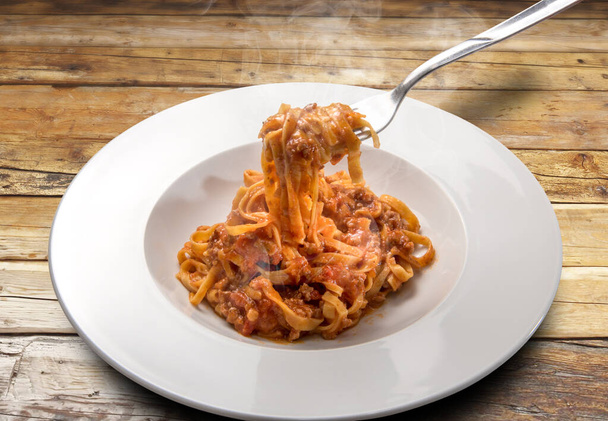 spaghetti op basis van eieren (Italiaanse tagliatelle) gegarneerd met vlees en tomatensaus, gestoomd in een plaat op rustieke houten ondergrond - Foto, afbeelding