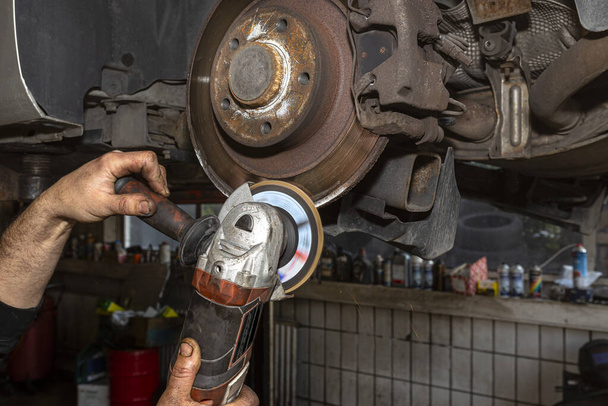 A mechanic grinds, with an angle grinder, the edge of an old rear brake disc in a car, regeneration of the brake system. - Photo, Image